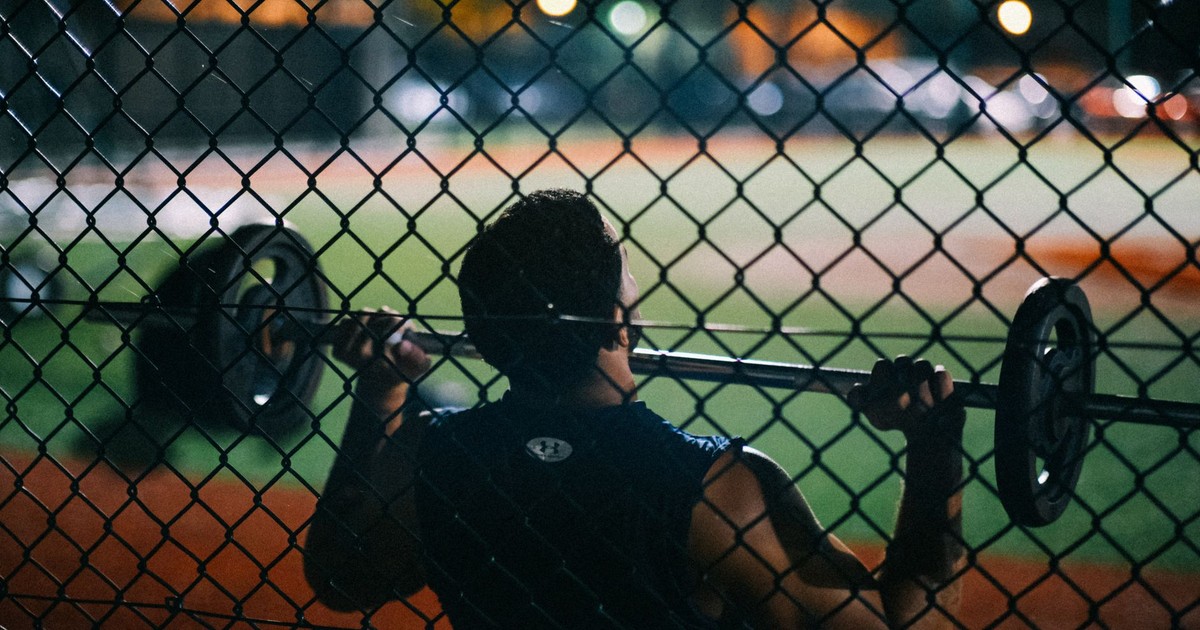 A man lifting weights behind a chain fence at night, showcasing strength and fitness.