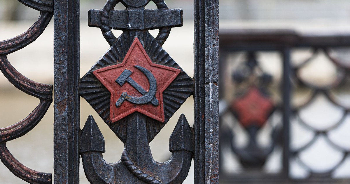 Close-up of an old iron fence featuring a Soviet anchor design with a red star and hammer and sickle symbol.