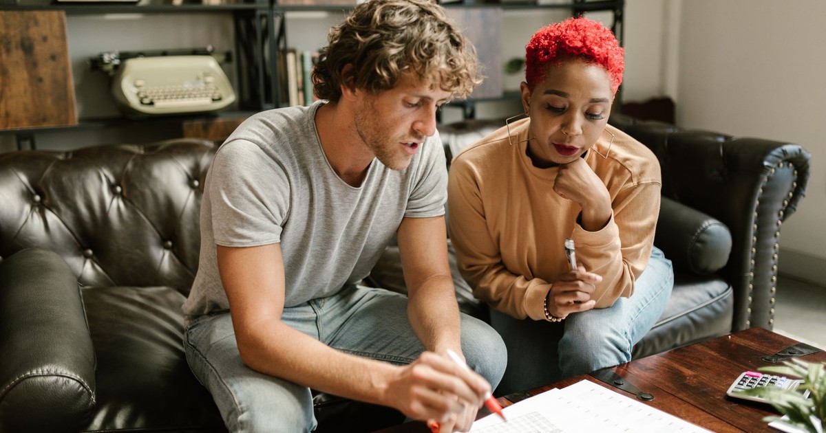 A couple sitting on a sofa examines documents in a cozy, modern living room setting.