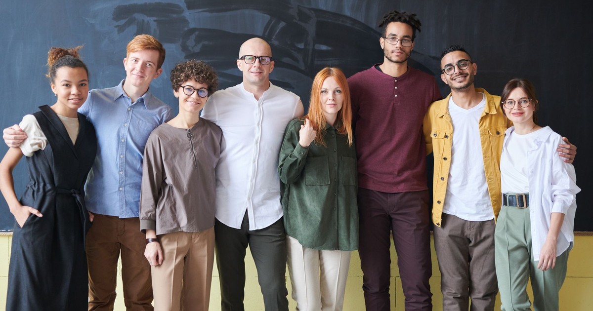 A diverse group of smiling adults posing in front of a chalkboard in an indoor setting.