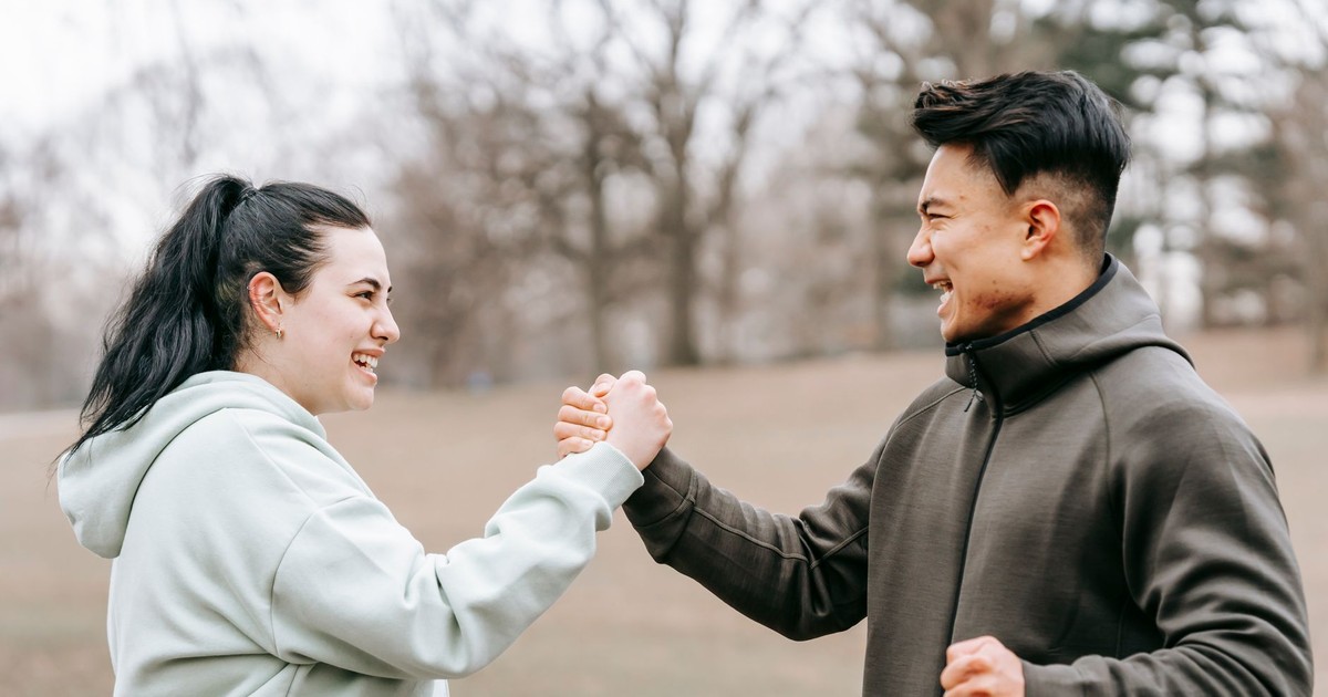 Side view of cheerful plus size female and ethnic instructor in activewear giving hands to each other on blurred background