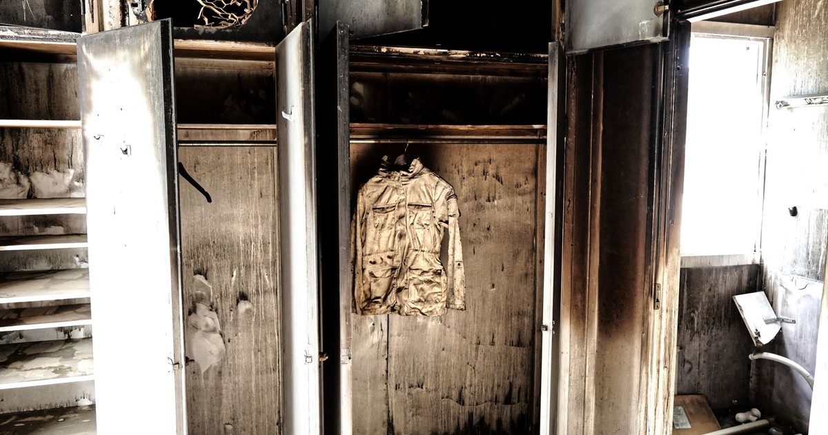 A haunting view of an abandoned, burned-out room with a decaying jacket hanging in a closet.