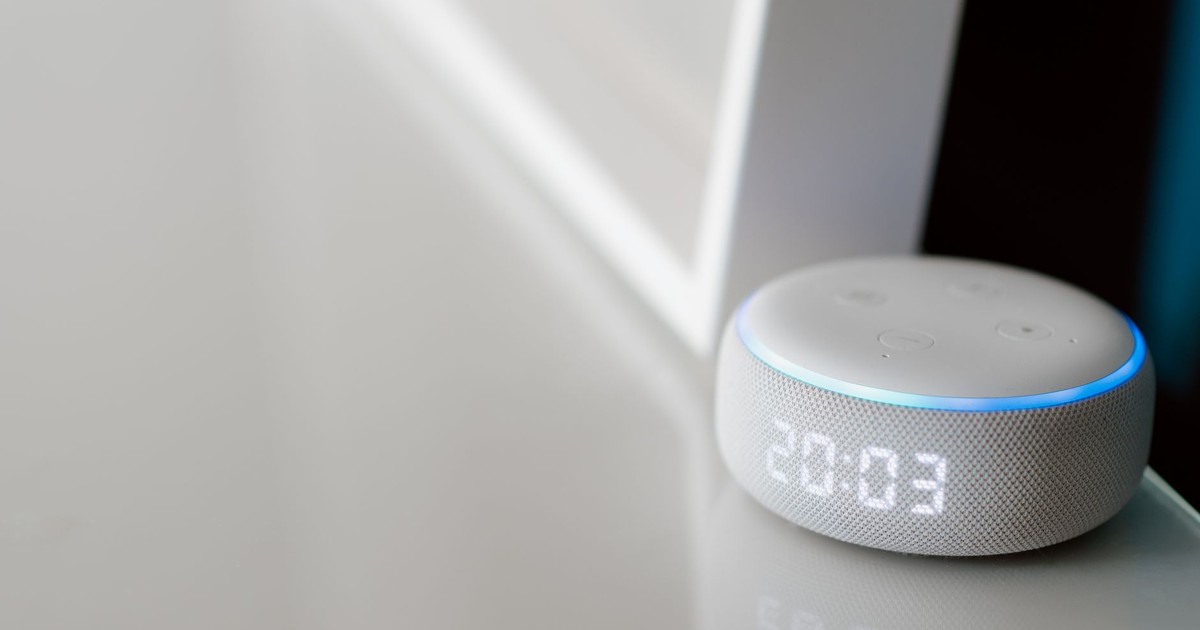 Close-up of a smart speaker with a digital clock display on a minimalist surface.