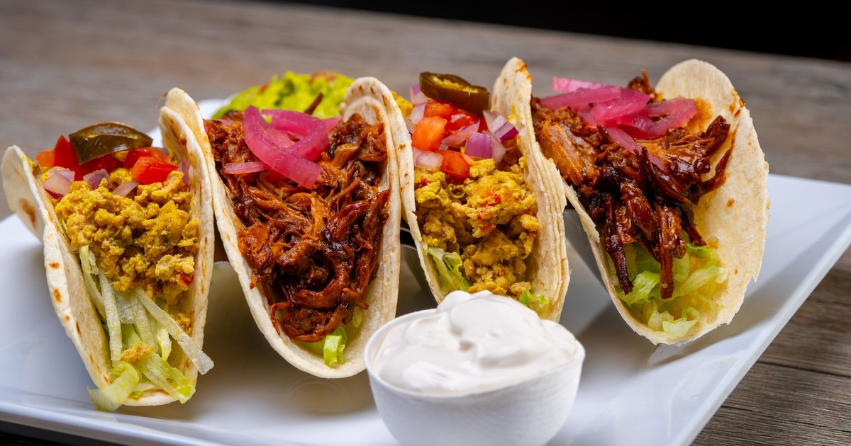 Four flavorful tacos with different fillings on a plate, perfect for a savory meal.