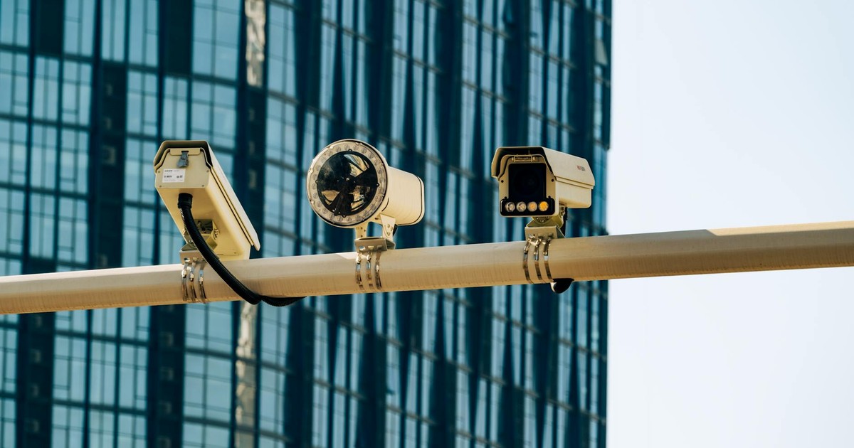 Surveillance cameras mounted on a pole in front of a modern glass building.