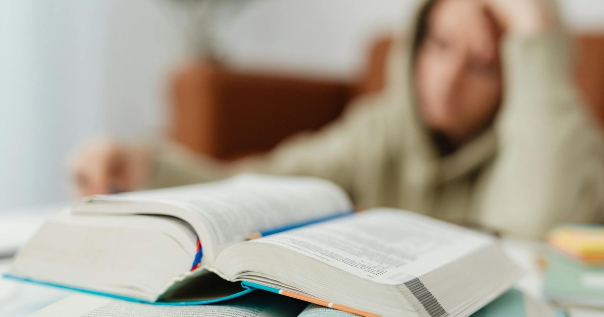 Blurred student studying at desk with open books, showcasing academic stress.