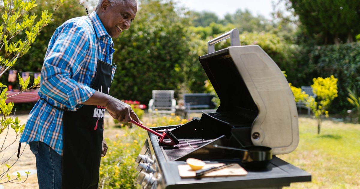 Elderly man enjoying barbecuing outdoors surrounded by greenery and garden ambiance.