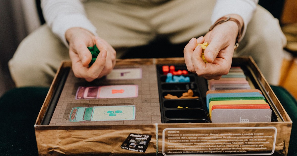 Person playing a board game with colorful pieces and cards indoors, focused and engaging.
