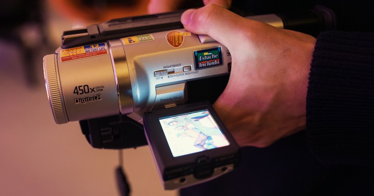 Close-up of a hand holding and operating a vintage digital camcorder with LCD screen.