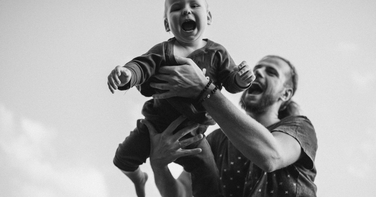 A father joyfully holds his happy baby boy in a lively outdoor setting.