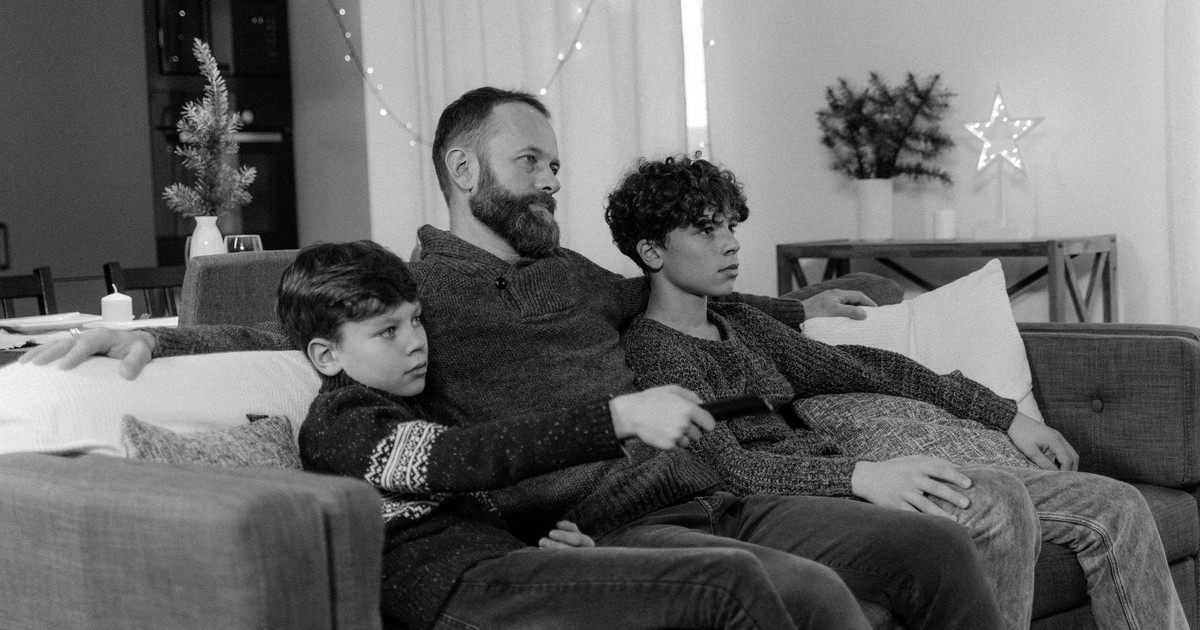 Father and sons enjoy a cozy movie night on the couch, experiencing togetherness.