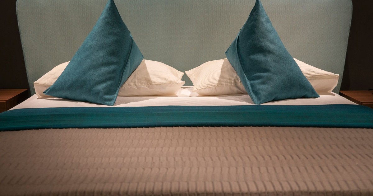 Modern minimalist bed with teal pillows and headboard, showcasing elegant interior design.