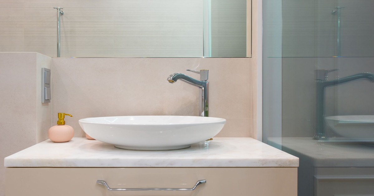 Interior of light modern washroom with sink and faucet on cabinet with decorative objects under mirror on wall next to glass wall