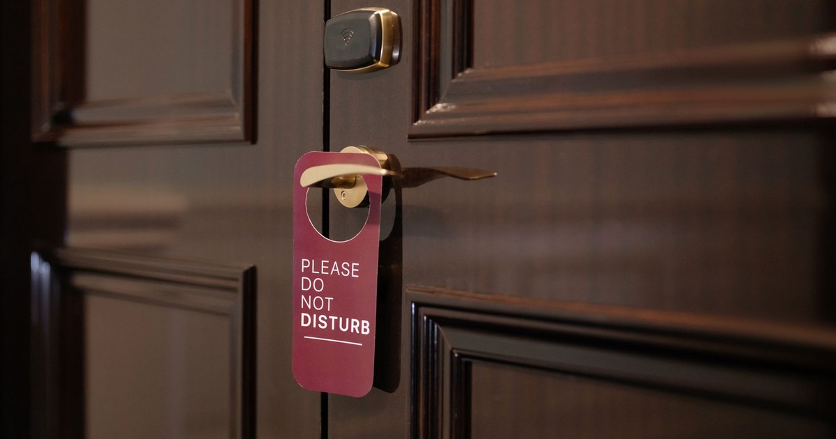 A wooden hotel door with a 'Please Do Not Disturb' sign hanging on the handle.