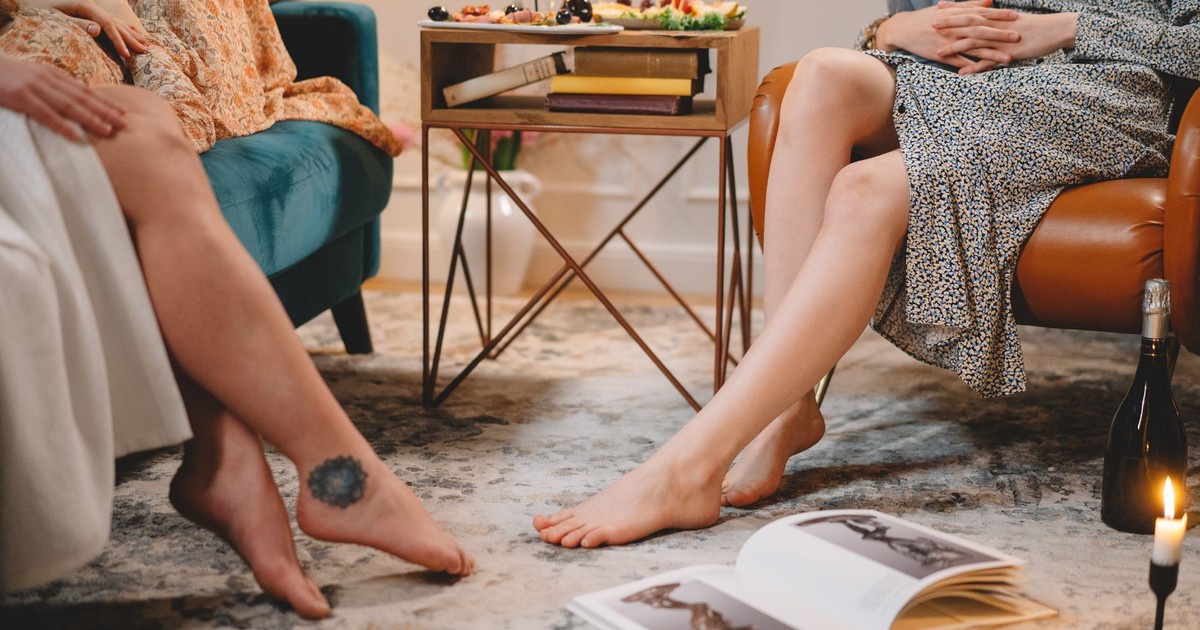 Women relaxing barefoot in a cozy living room with snacks and books.