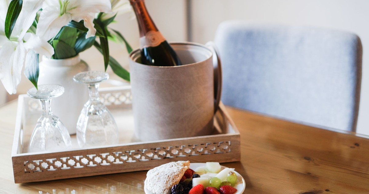 Elegant hotel arrangement with champagne, fruits, and white lilies on a wooden tray.