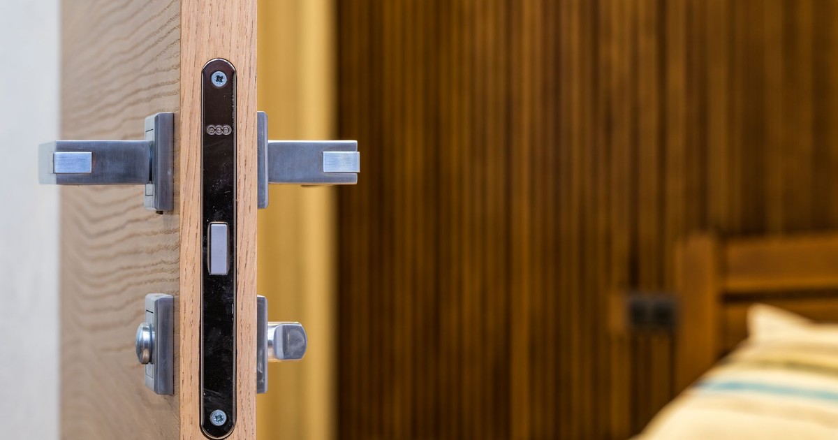 Opened doorway with lock and simple metal handle in light room with wooden bed