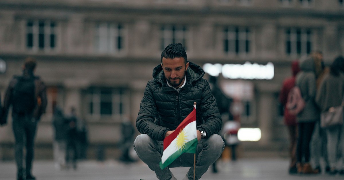 Male sitting on city square near memorial with Kurdistan national flag and flowers