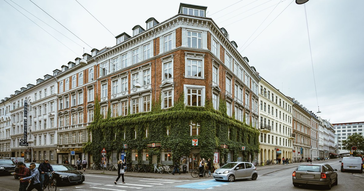 City street scene with historic buildings, ivy, and pedestrians in an overcast urban setting.