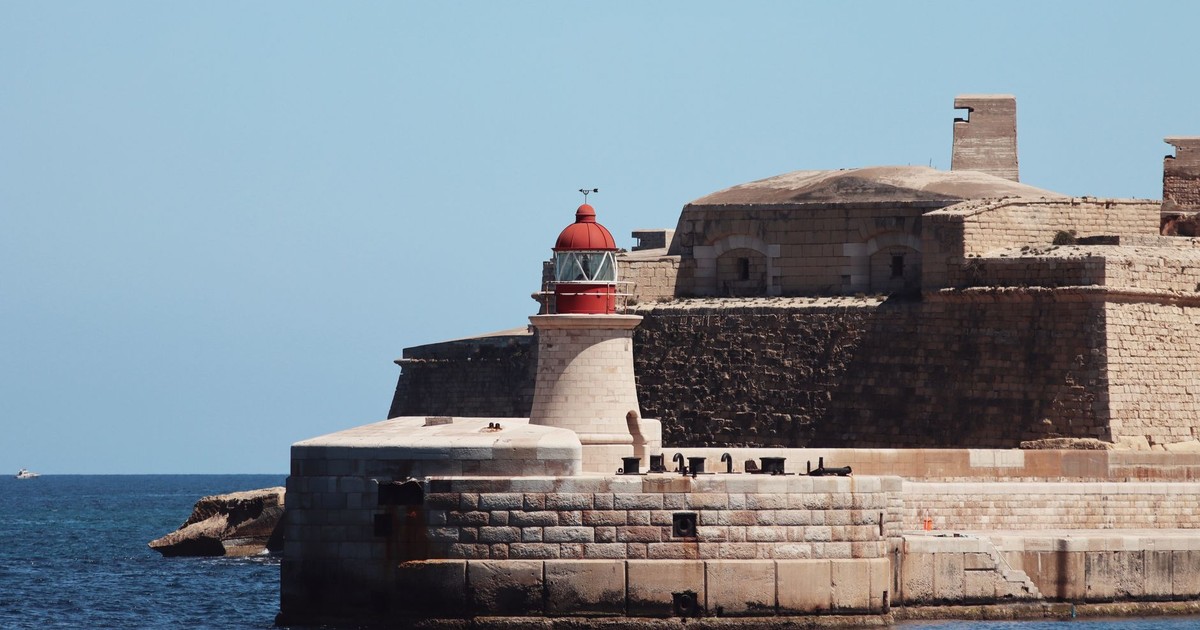 A striking lighthouse stands by ancient fortifications on the seaside at Valletta, Malta.