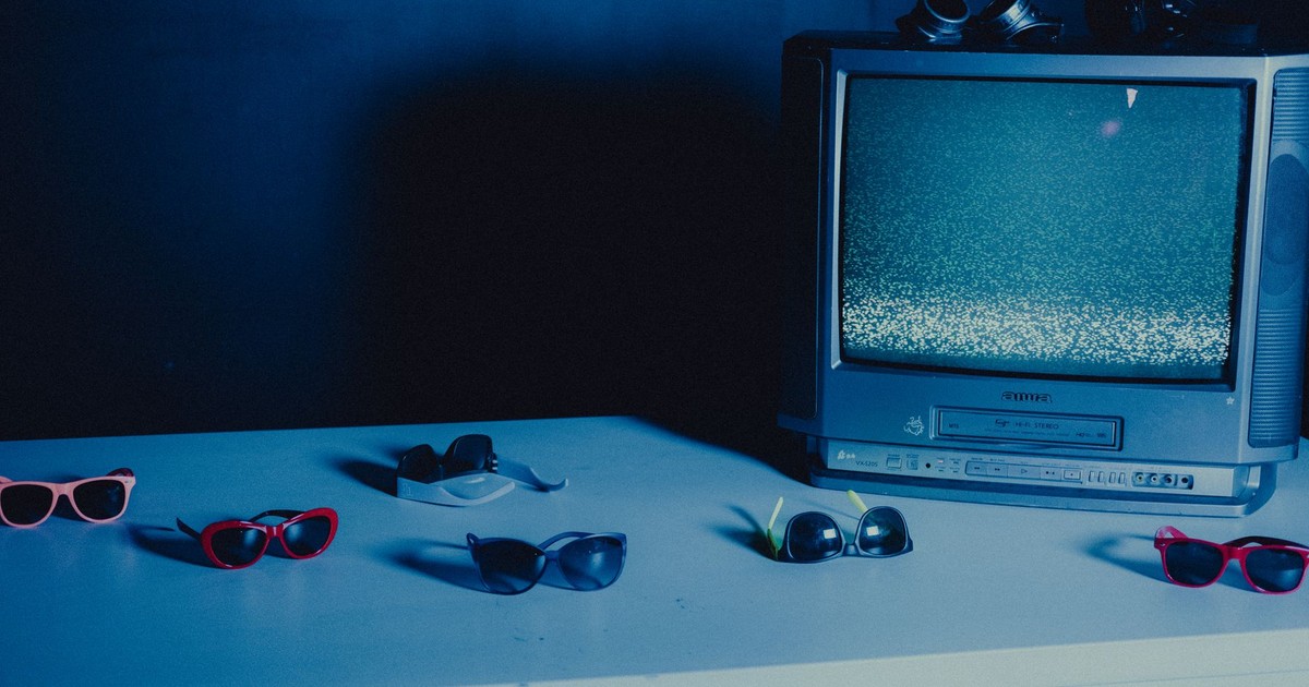 Vintage television with static display surrounded by colorful sunglasses on a blue-lit table.