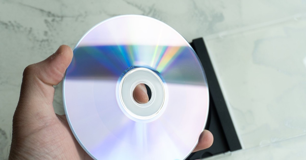 Close-up of a person holding a reflective CD disc with a transparent case on a marble background.
