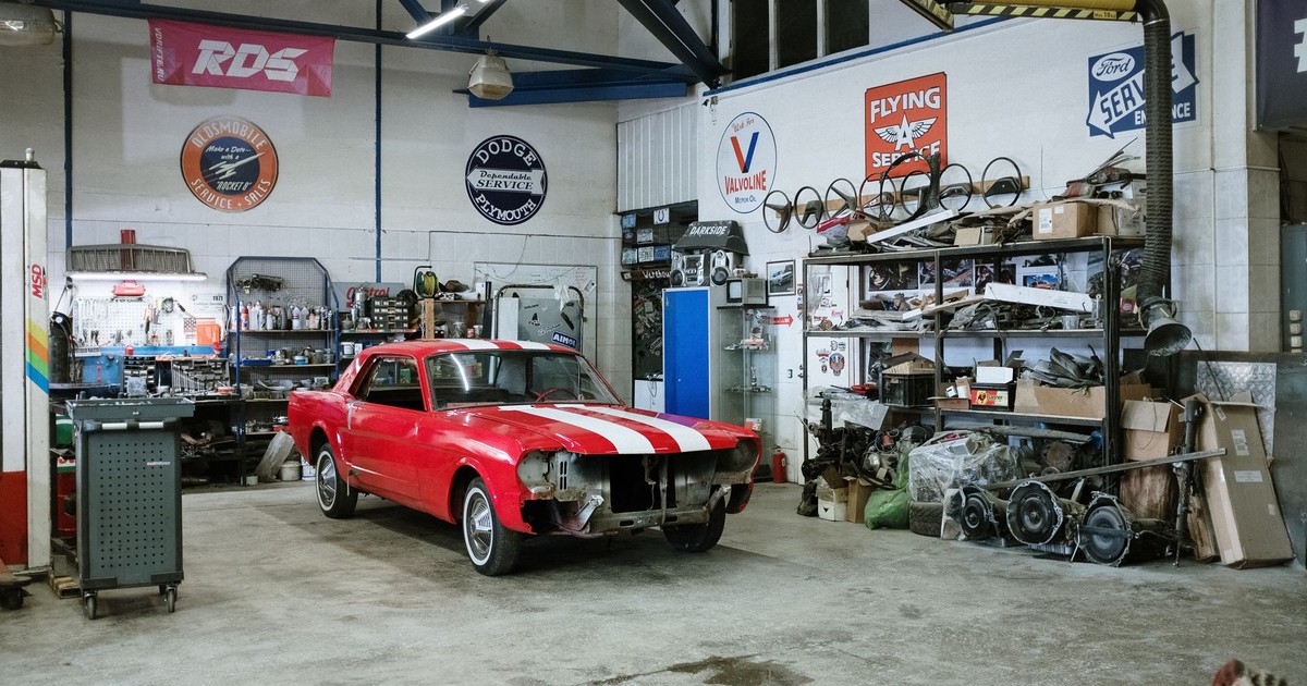 A vintage red car undergoing restoration in a well-equipped workshop with various tools and auto parts.