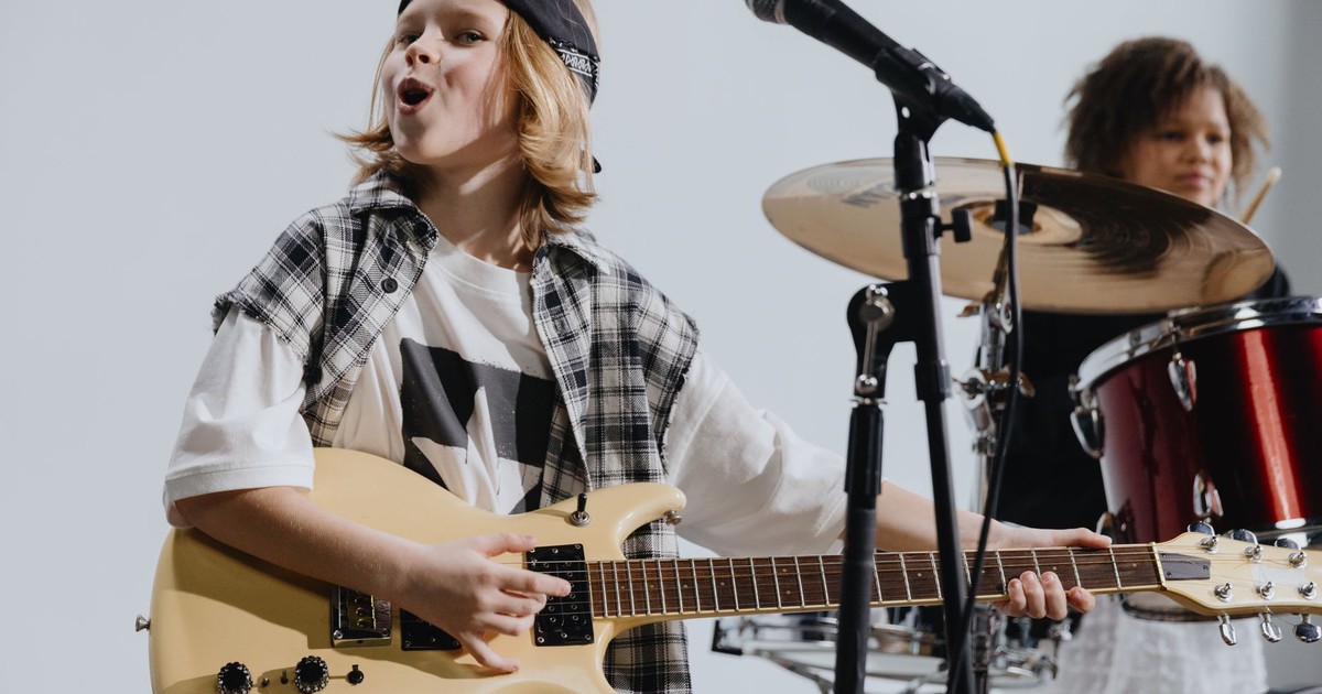 Young musicians passionately playing electric guitar and drums on stage, showcasing kids' musical talent.