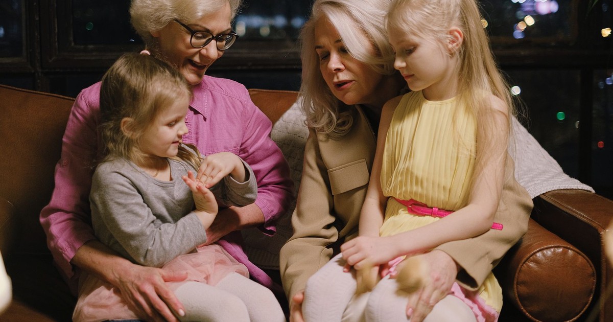 A warm family moment indoors with two grandmothers and two granddaughters sitting together on a sofa.