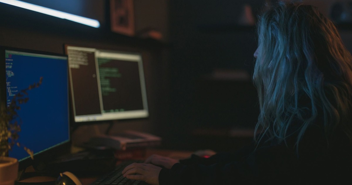 A woman working on programming tasks with multiple screens in a dimly lit room.