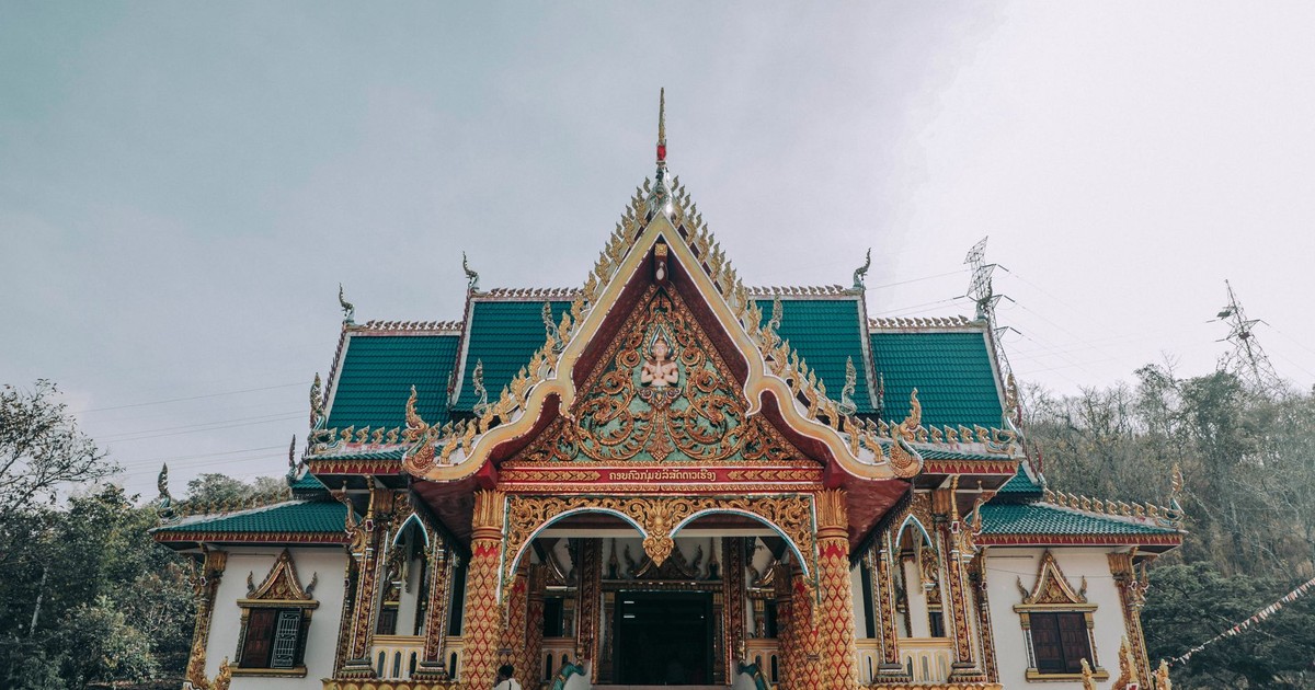 Low angle of old stone Buddhist church facade with ornament behind trees in city
