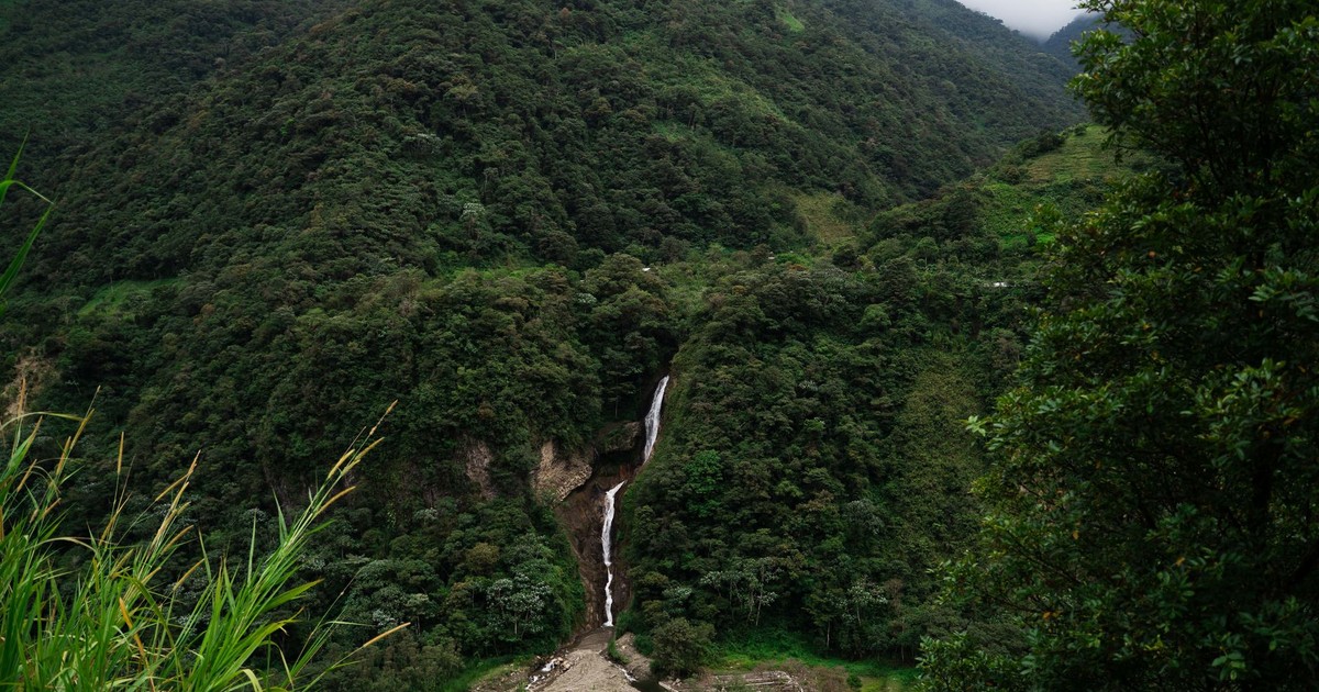 Lush green mountains and a stunning waterfall in Banos, Ecuador create a tranquil nature scene.