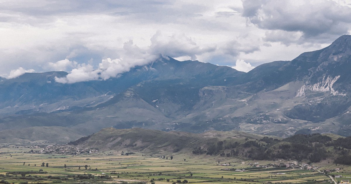 Panoramic view of green valley and majestic mountains under cloudy sky.