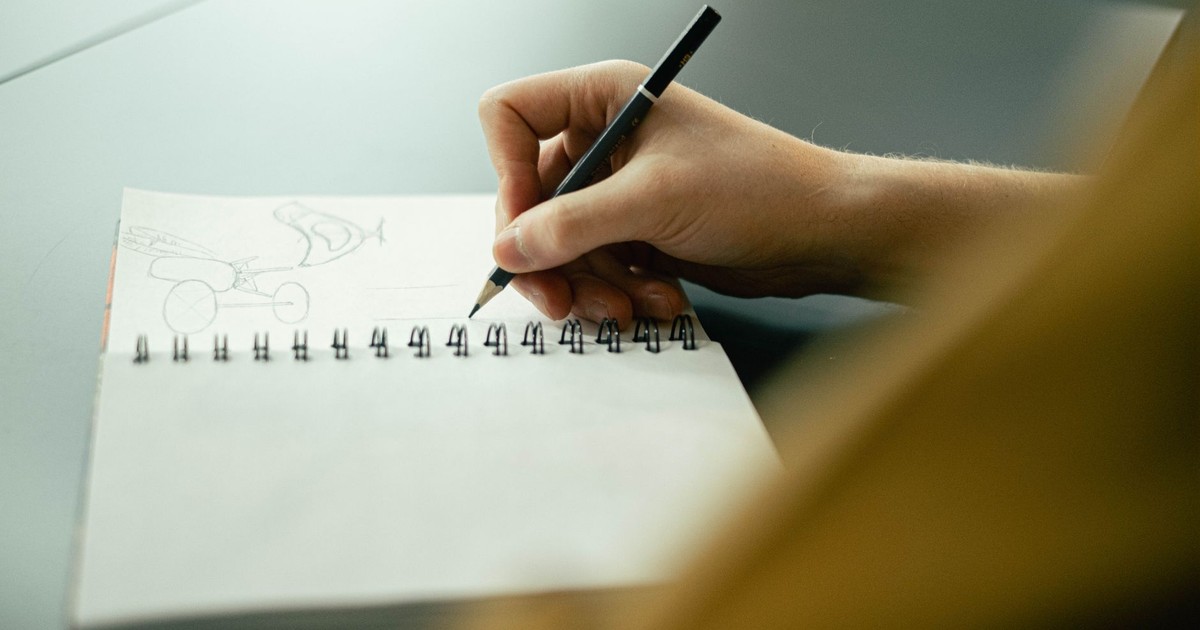 Hand sketching in a notebook with a pencil, focusing on creativity and planning.