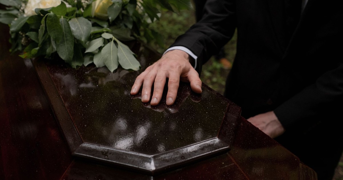 A hand placed on a coffin with flowers, symbolizing loss and mourning.