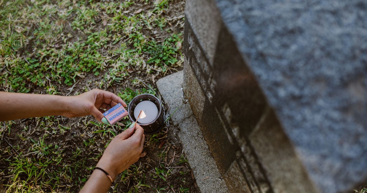 Close-up of hands lighting a candle next to a tombstone in a cemetery.