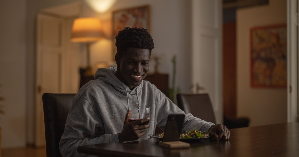 Smiling man having dinner and wine while using his smartphone indoors. Relaxed evening ambiance.