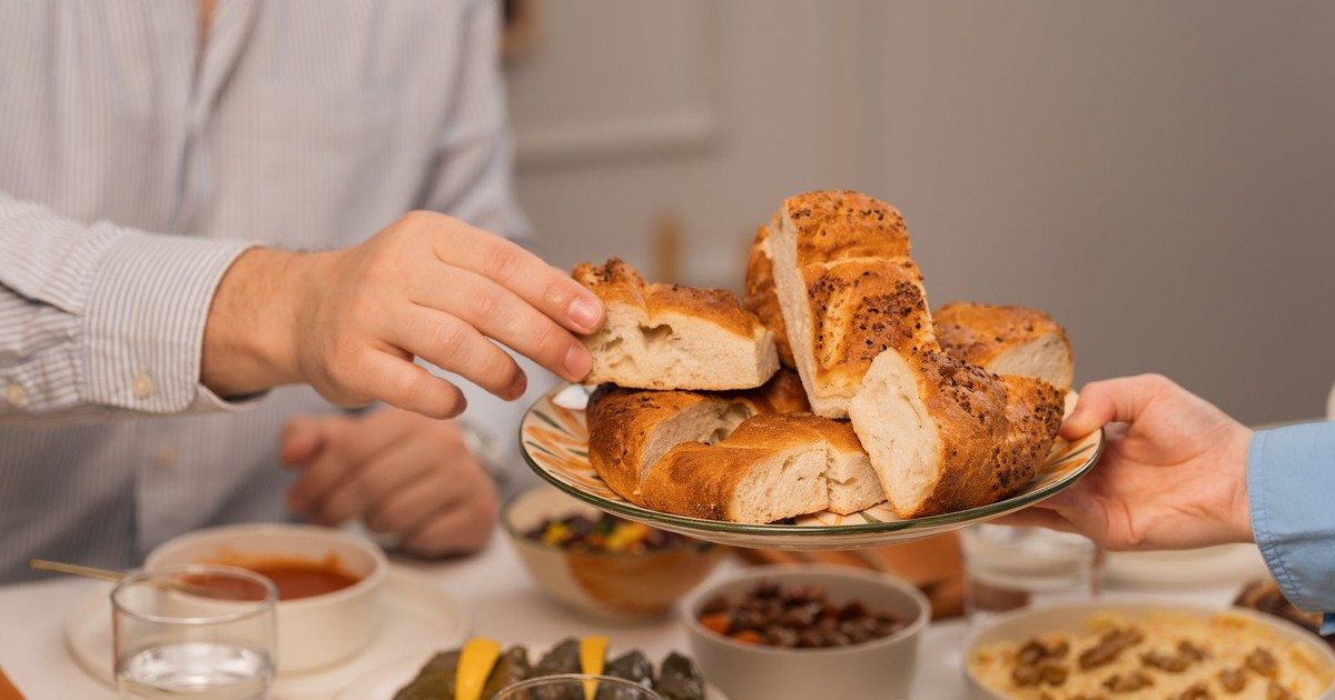Hands exchanging fresh bread at a dinner table filled with diverse dishes and drinks.