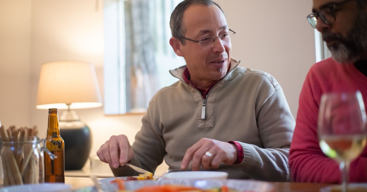 Two men enjoying a casual dinner conversation indoors with wine and snacks, capturing a warm and friendly atmosphere.
