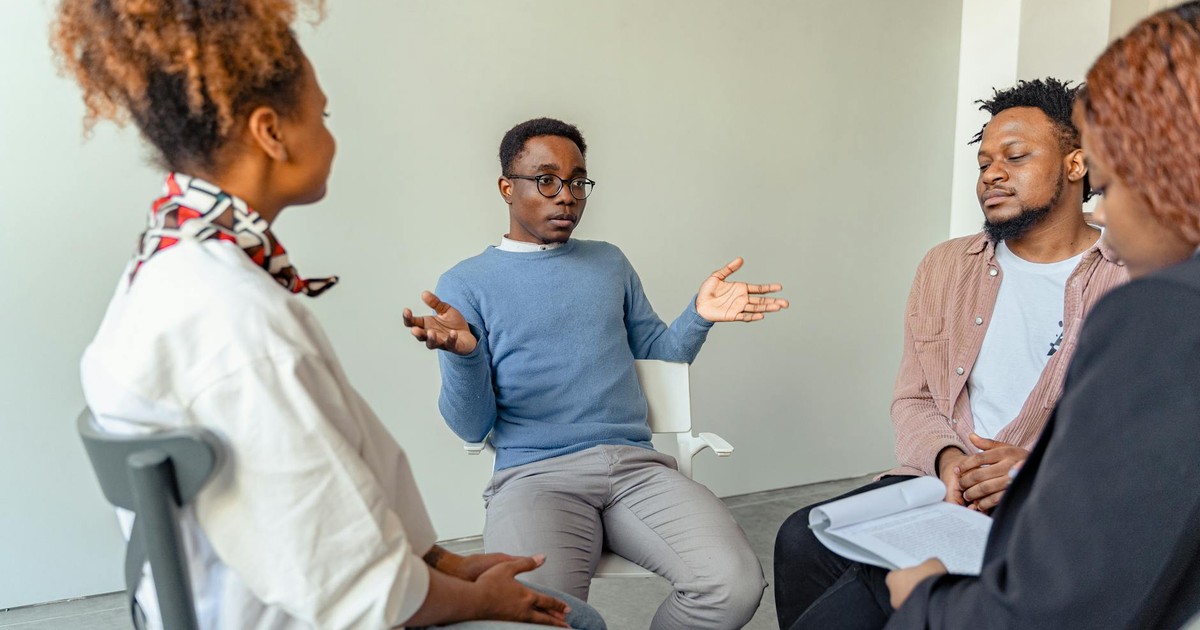 Diverse group therapy session with young adults and a mental health professional indoors.