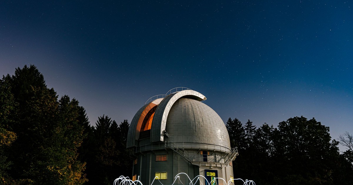 A scenic view of an observatory with a star-filled sky at night, surrounded by trees.