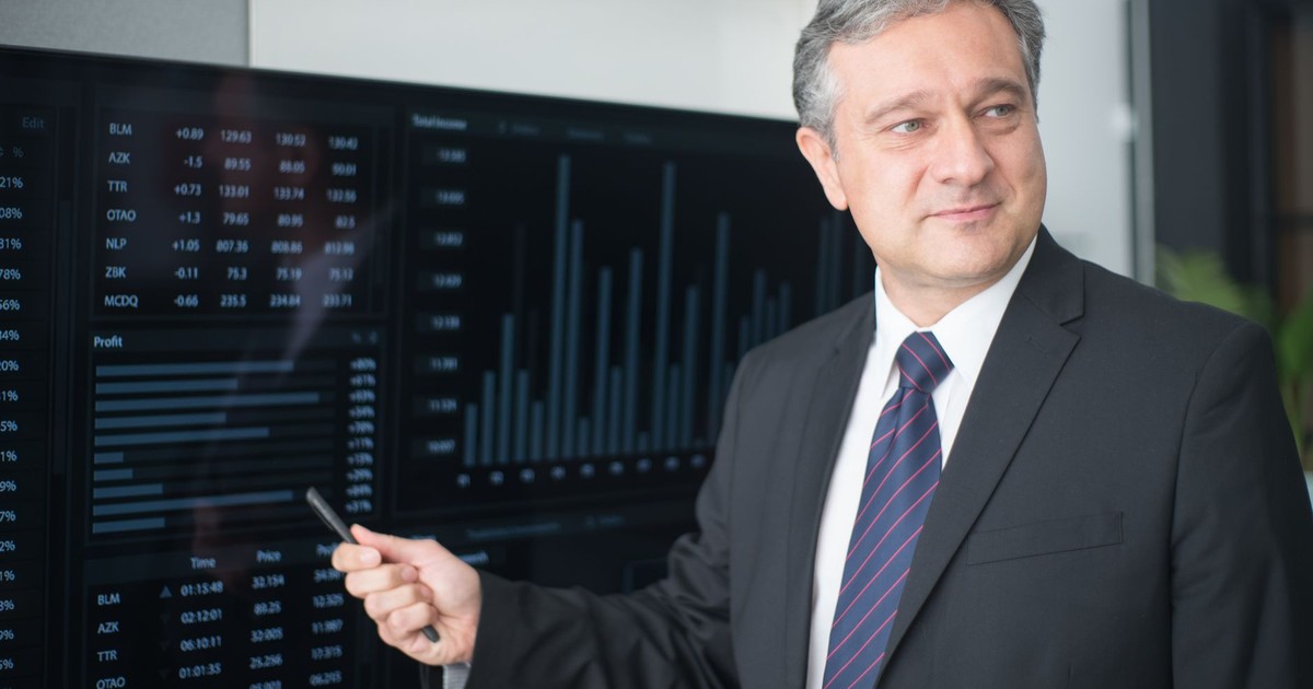 Professional man in suit reviewing financial charts on monitor, showcasing stock market trends.