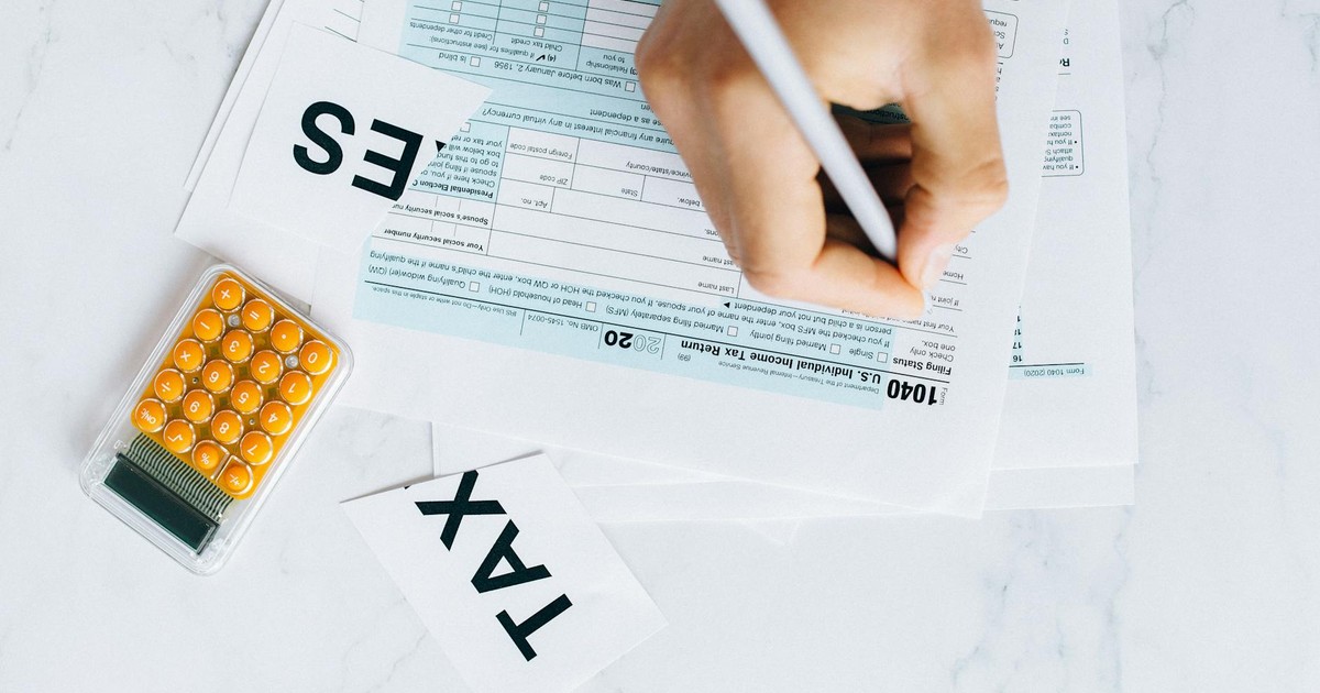 Close-up of hand writing on tax form with calculator nearby on white surface.