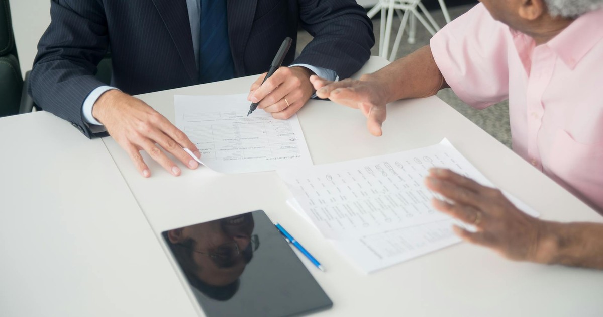 A business meeting between an elderly client and a consultant discussing documents at an office table.