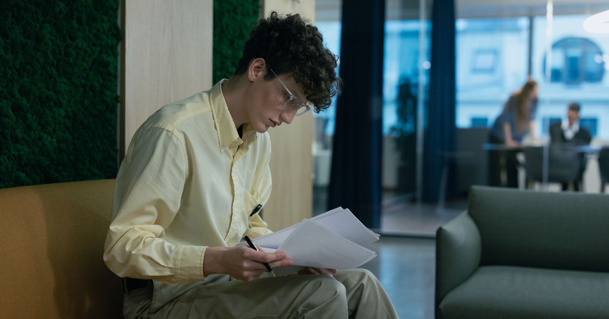 A focused young professional reading documents on a couch in a modern office environment.