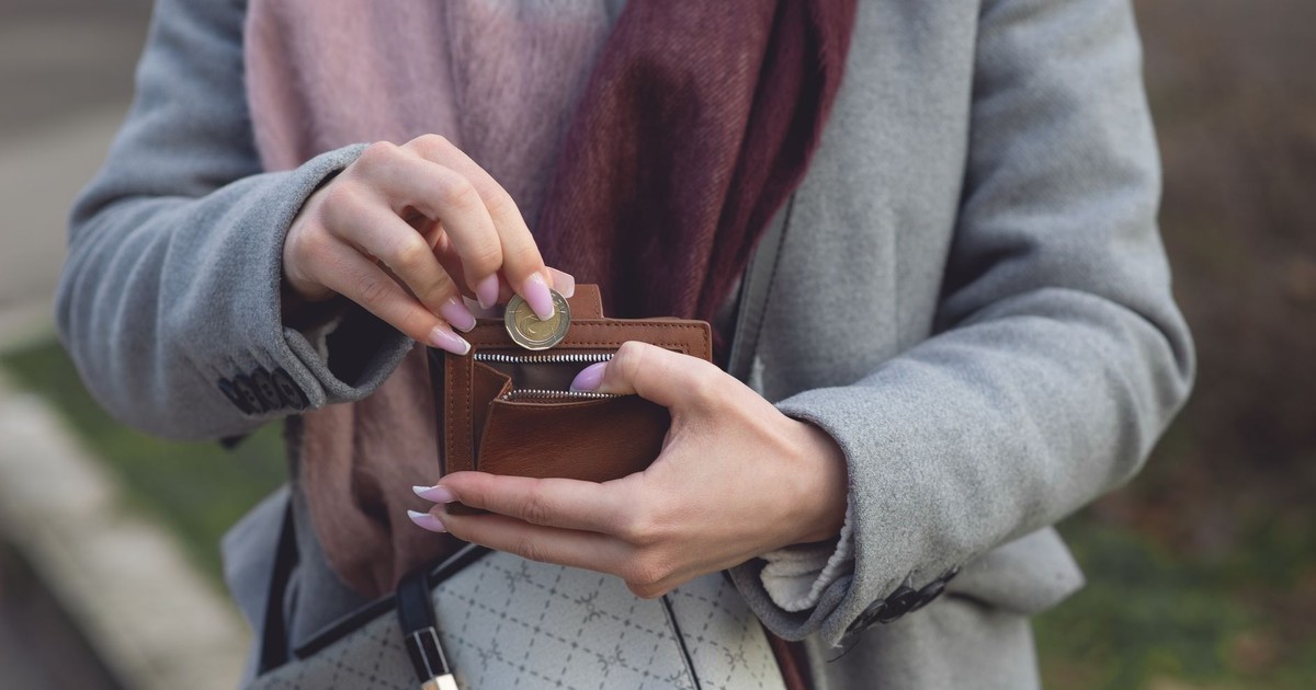 Close-up of a woman placing a coin into a wallet while outdoors, wearing a coat and scarf.