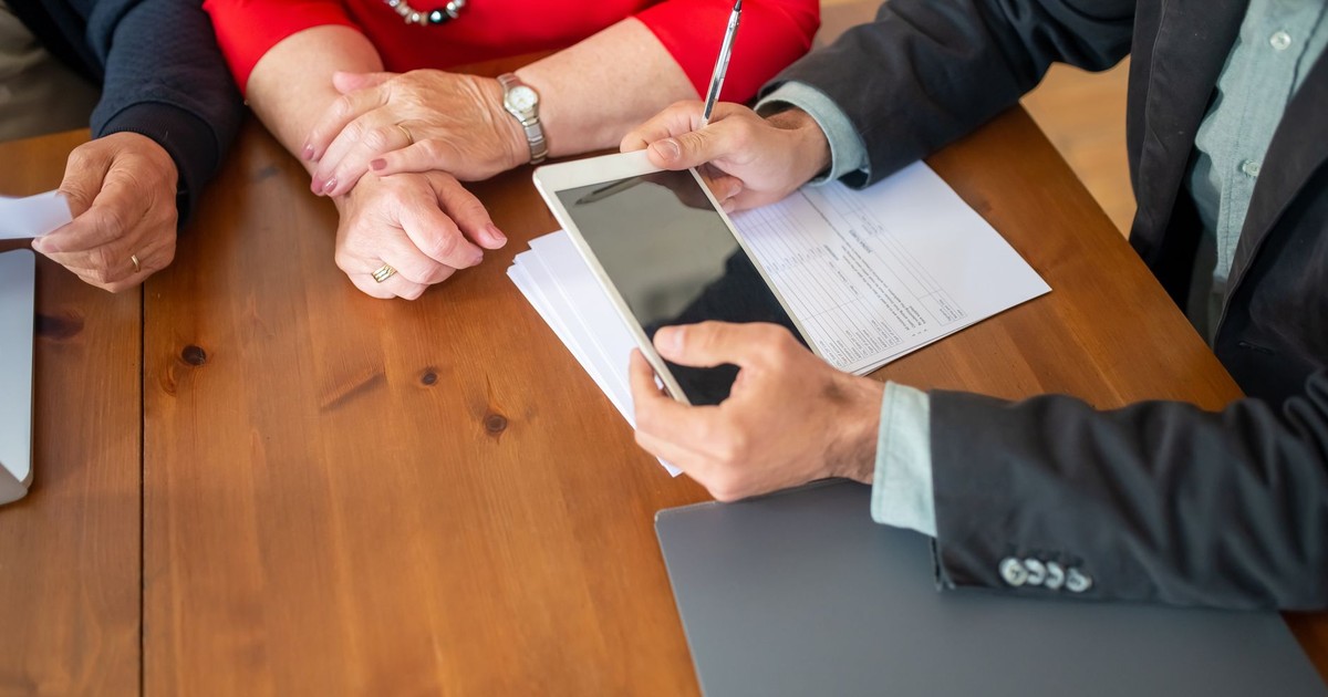 Business meeting at a wooden table with consultant reviewing documents and using a digital tablet.