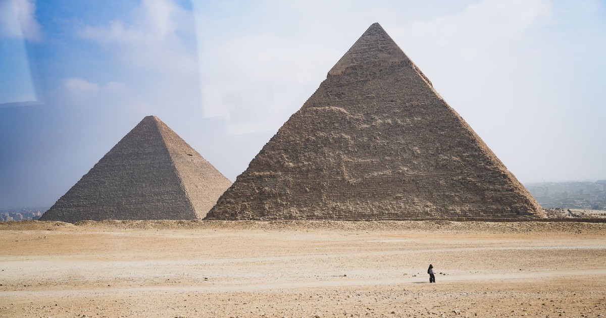 Wide shot of the Pyramids of Giza at daytime with a distant solitary figure.