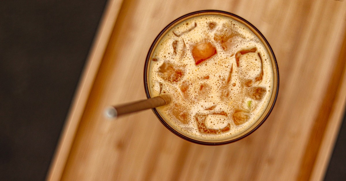 A top view of iced coffee with paper straw on a wooden tray, ideal for coffee enthusiasts.