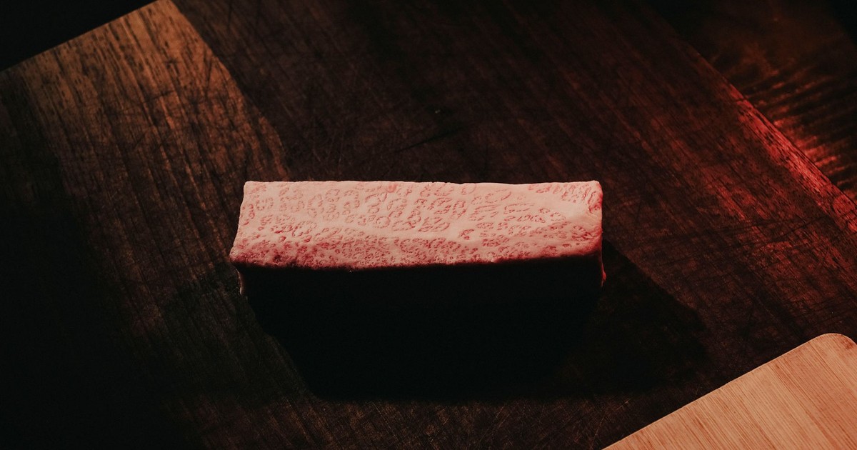 Close-up of marbled Wagyu beef on a rustic dark wooden table, showcasing rich texture and color contrast.